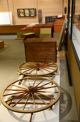 手前の車輪は、たばこ荷車の車輪です。奥の箱は、たばこ製品を入れる箱です。